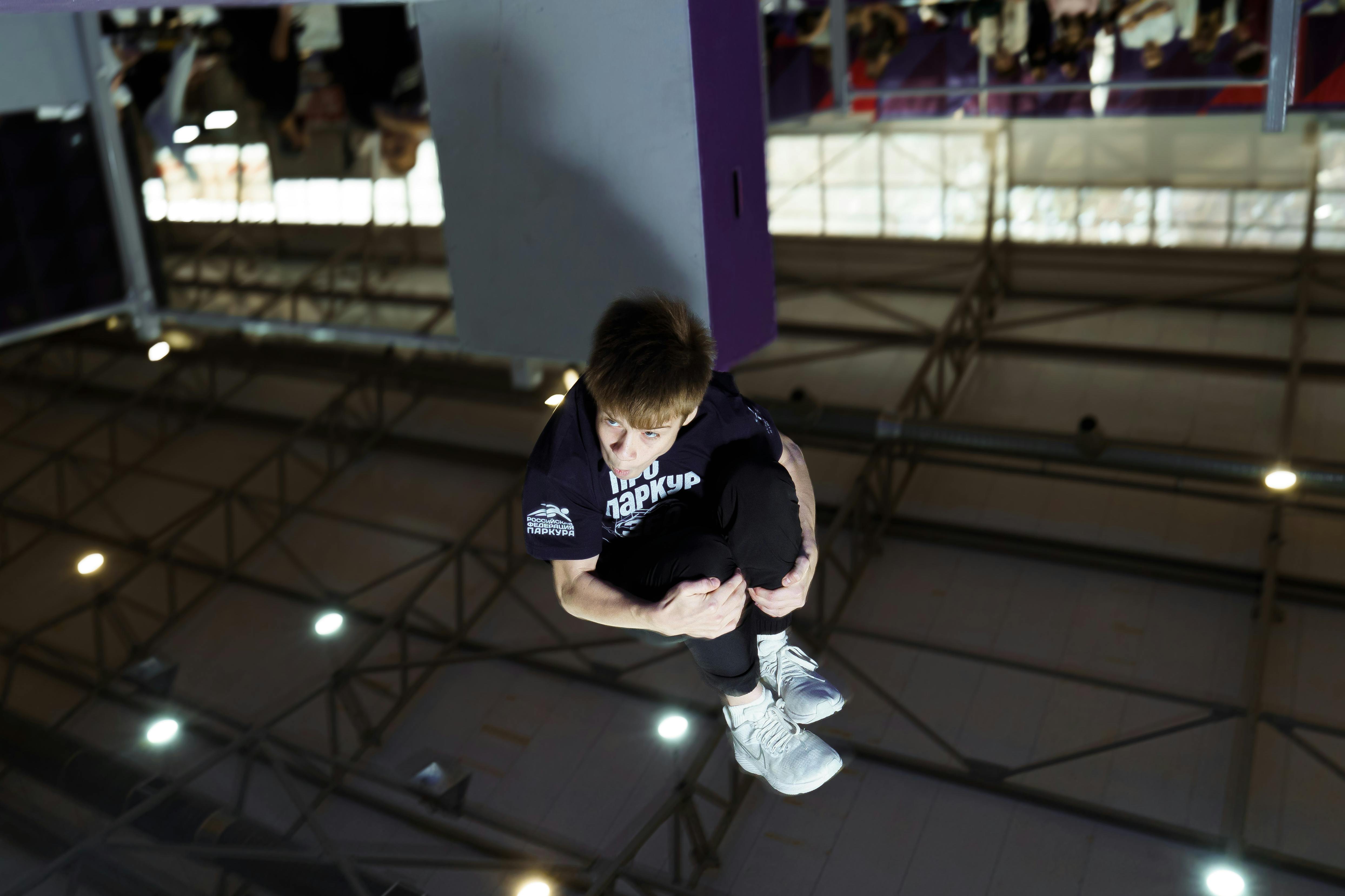 grátis Um jovem executa um salto mortal de parkour em ambiente fechado, demonstrando habilidades atléticas e agilidade. Foto profissional
