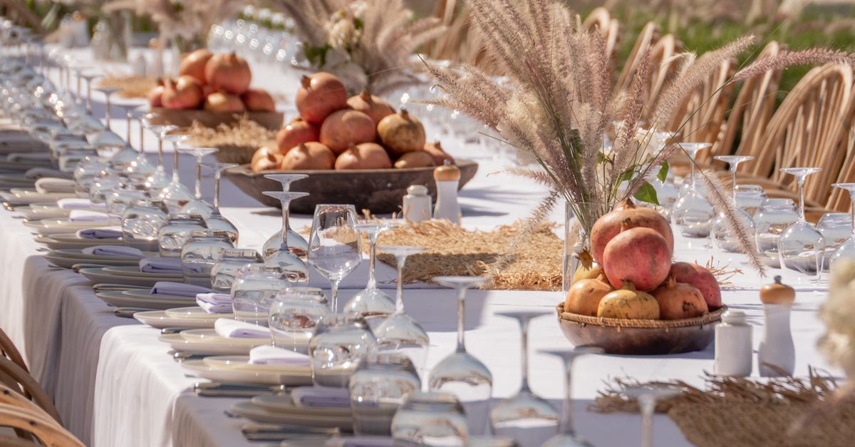 Long banquet table with elegant setup featuring pomegranates and glassware, perfect for an outdoor celebration.