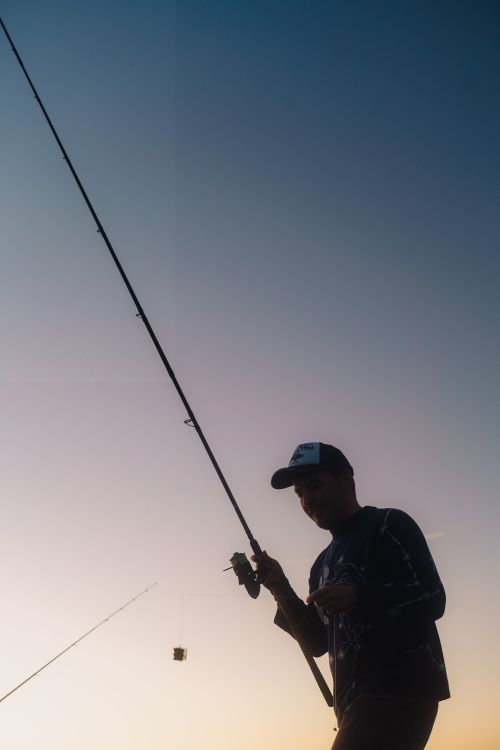 Free A silhouette of a fisherman casting a line during a serene sunset, showcasing tranquil outdoor activities. Stock Photo