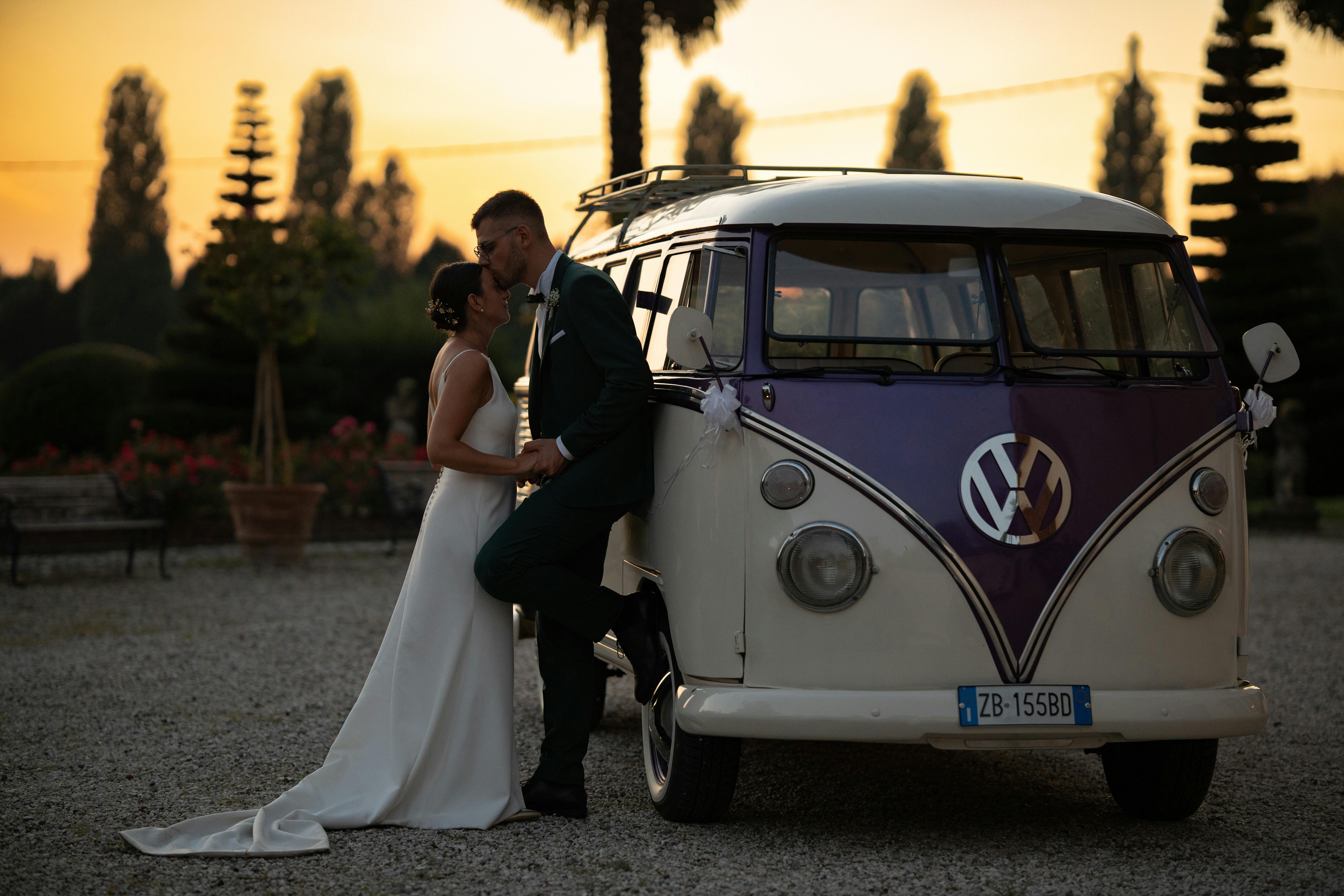 Newlyweds embrace by a vintage VW bus at sunset in Venice, Italy. Perfect blend of romance and classic style.