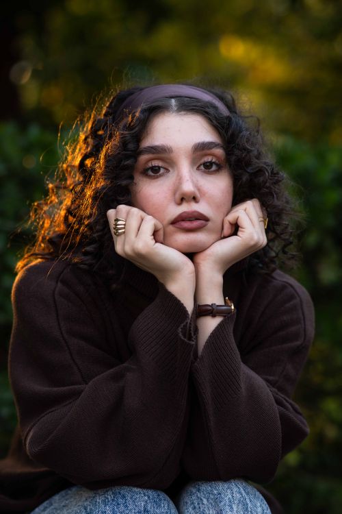 Free A contemplative woman with curly hair enjoys a serene moment outdoors at sunset. Stock Photo