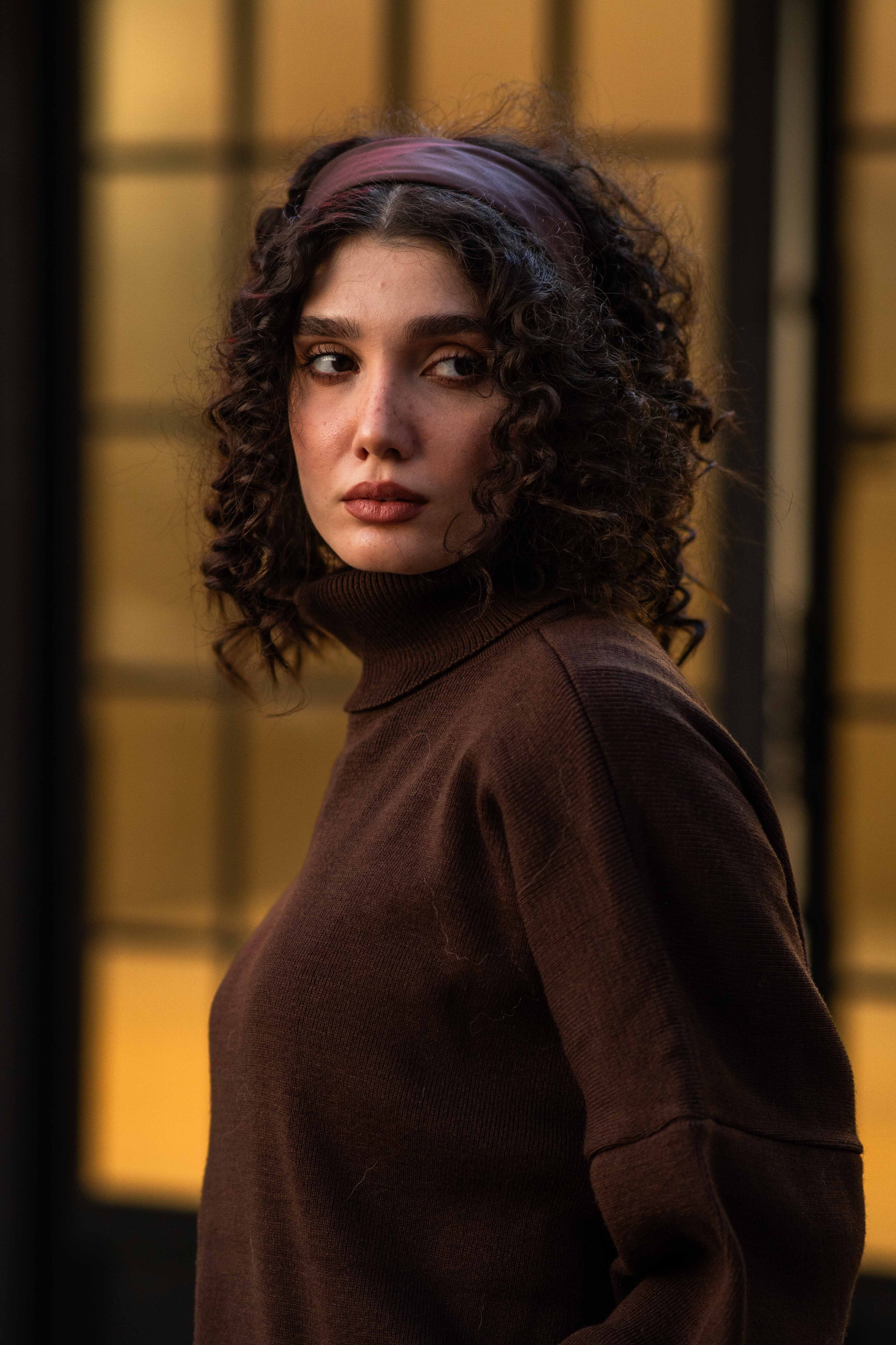 Elegant portrait of a woman with curly hair in a brown sweater, looking contemplative.