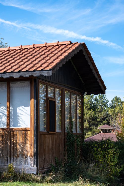 Free A cozy rustic wooden cottage with a tiled roof in a sunny forest area. Stock Photo
