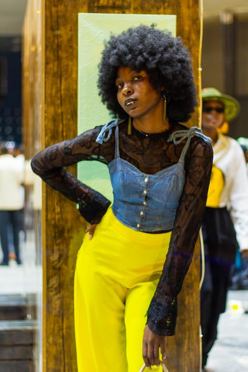 Free Fashionable woman with afro hair in denim top and yellow pants posing confidently indoors. Stock Photo