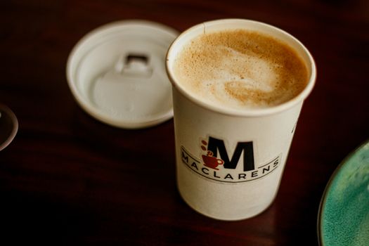 A steaming cup of coffee in a branded Maclarens takeaway cup on a cafe table in Dhaka, Bangladesh.