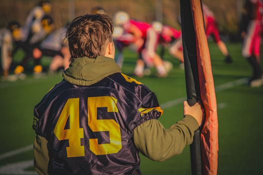 A young football player stands on the sidelines during a team match.