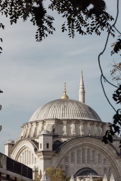 Free Serene view of a mosque with a golden dome framed by trees in daylight. Stock Photo