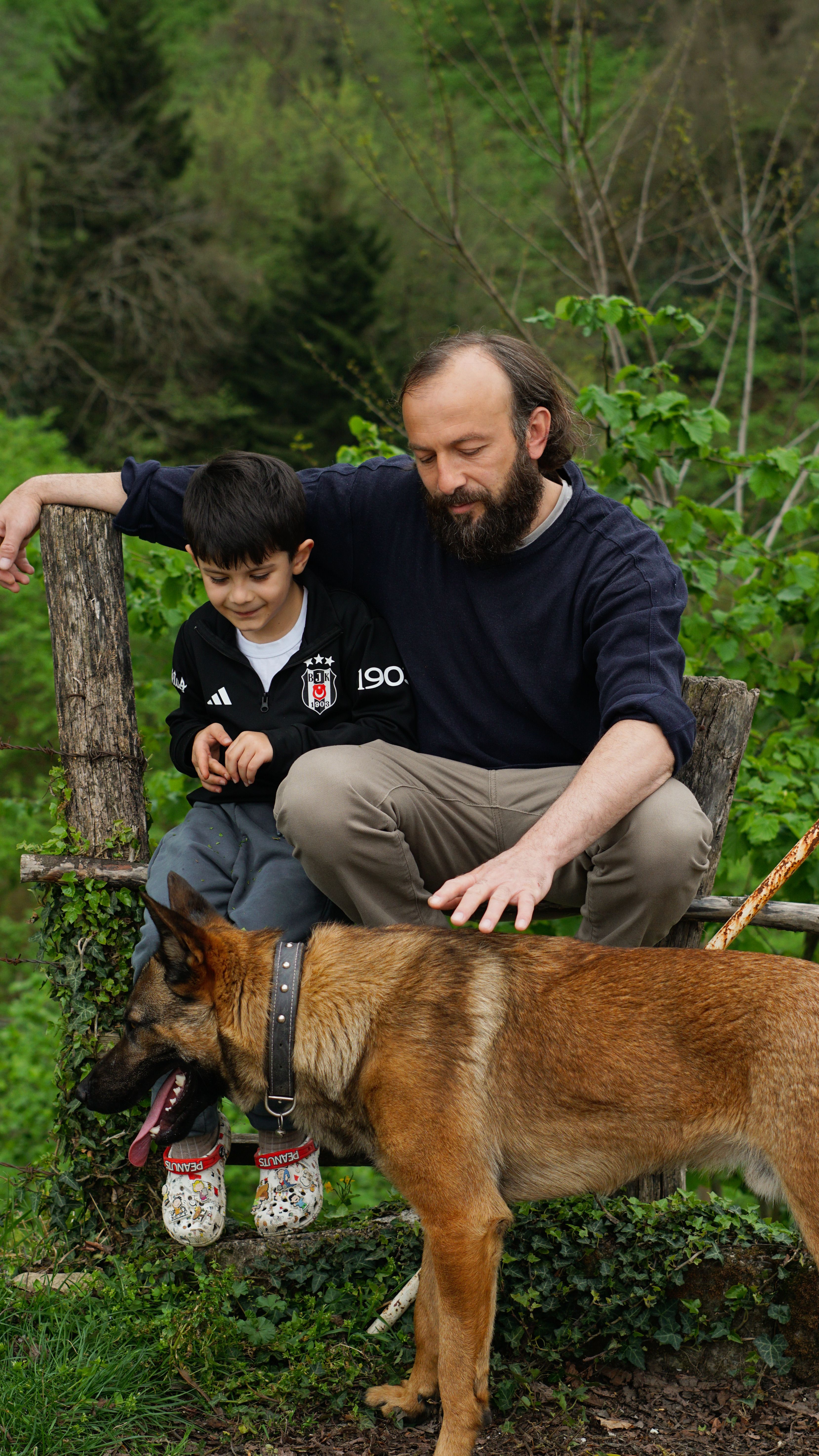 A father and son enjoy quality time outdoors with their dog on a lush green day.