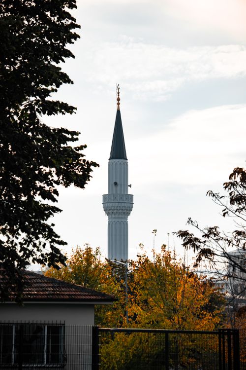 Free A tall, elegant minaret framed by autumn trees against a cloudy sky. Stock Photo