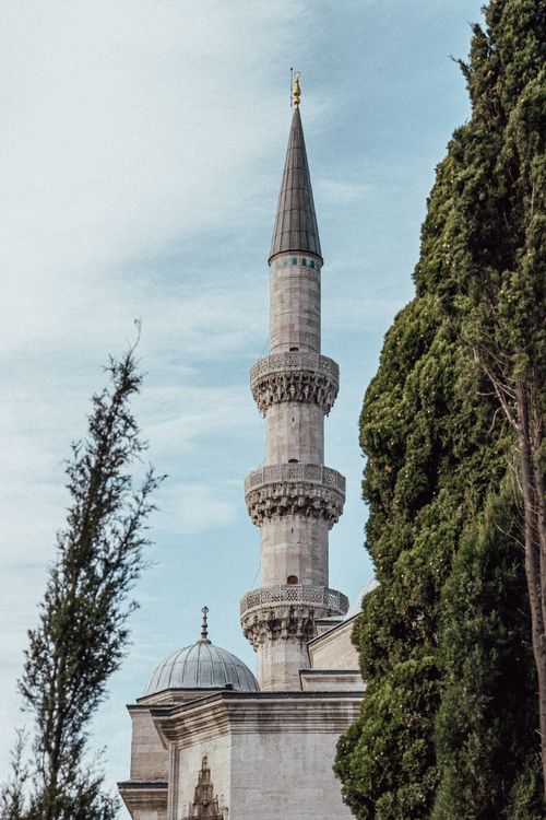 Free A beautiful mosque minaret in Istanbul contrasted against a clear blue sky and framed by lush greenery. Stock Photo