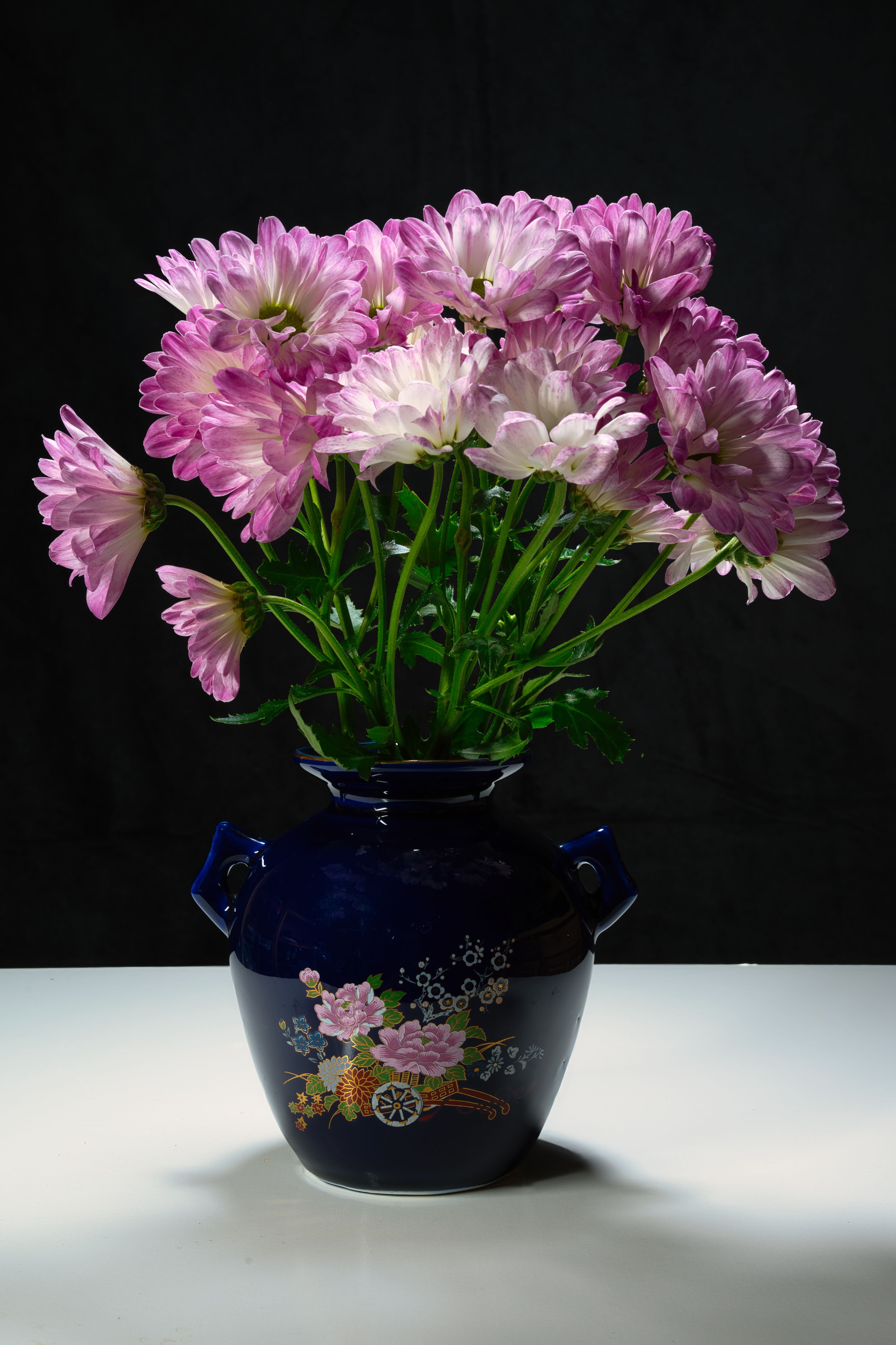 [ColoSach]-a-bouquet-of-purple-and-white-chrysanthemums-in-an-ornate-vase-with-floral-design-on-a-reflective-surface.