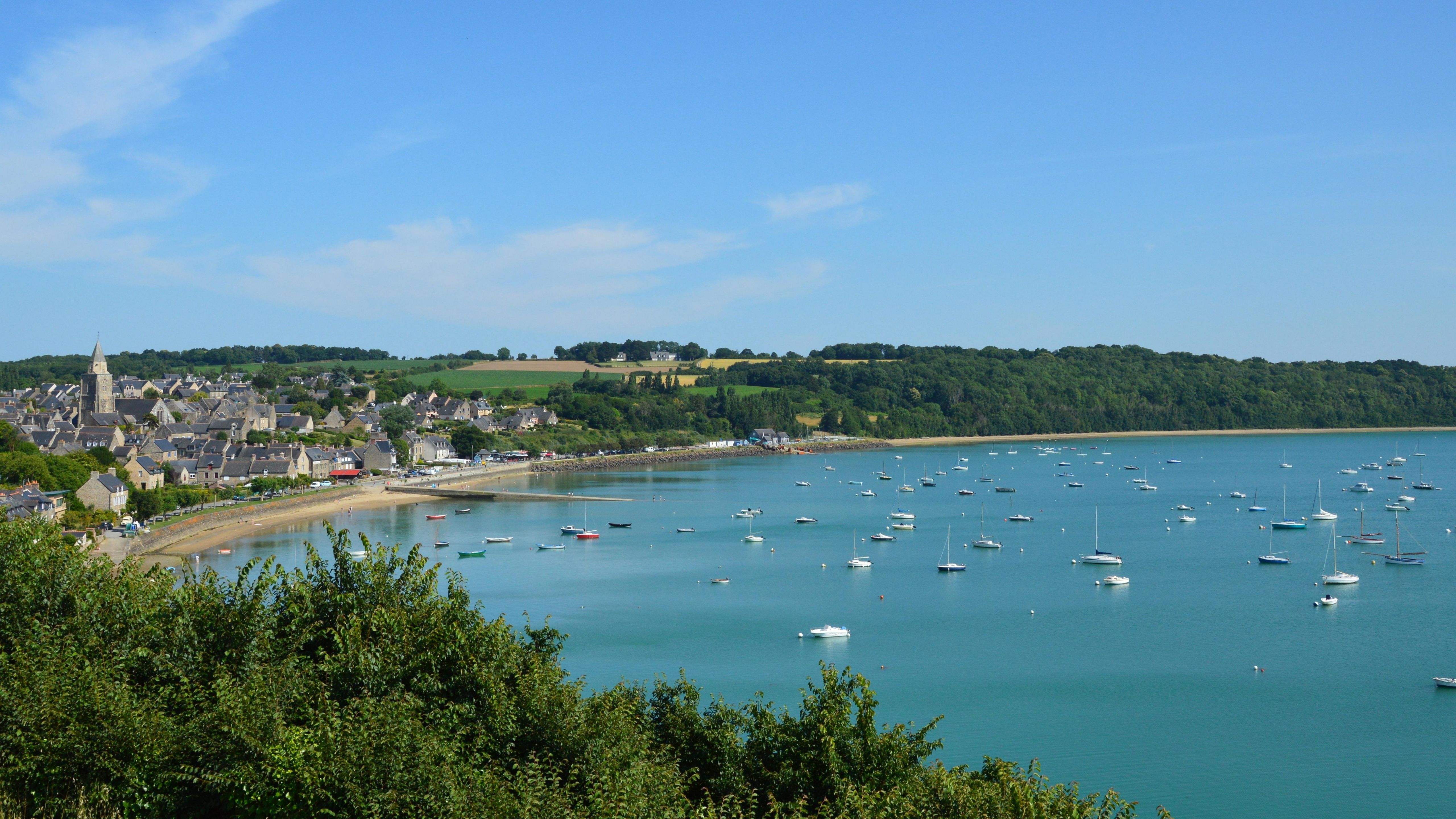 Vue pittoresque du port de Saint-Suliac, en France, avec ses bateaux et sa végétation luxuriante sous un ciel bleu azur.