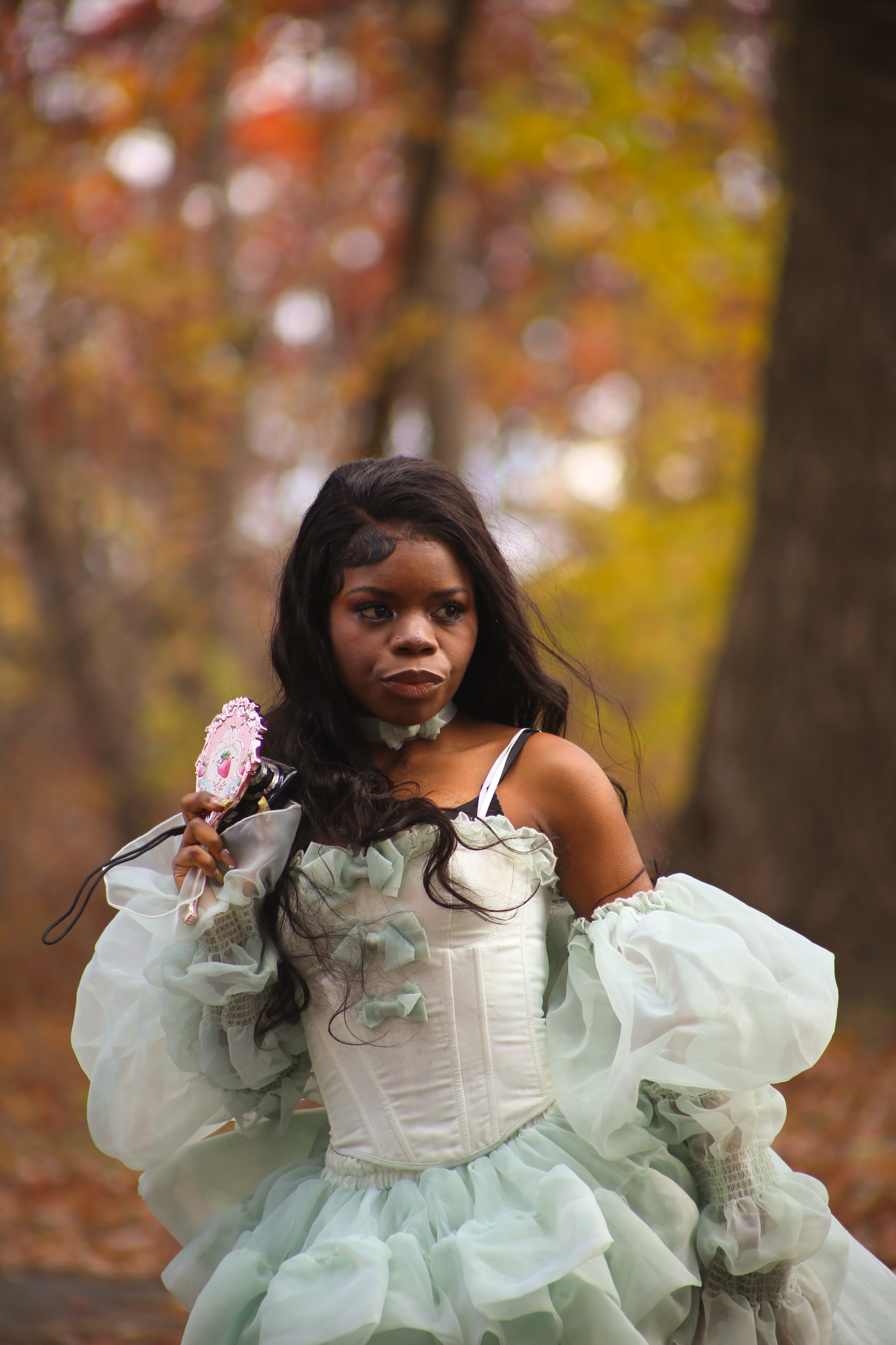 Young woman in a fantasy costume holding a mirror in an autumn forest setting.