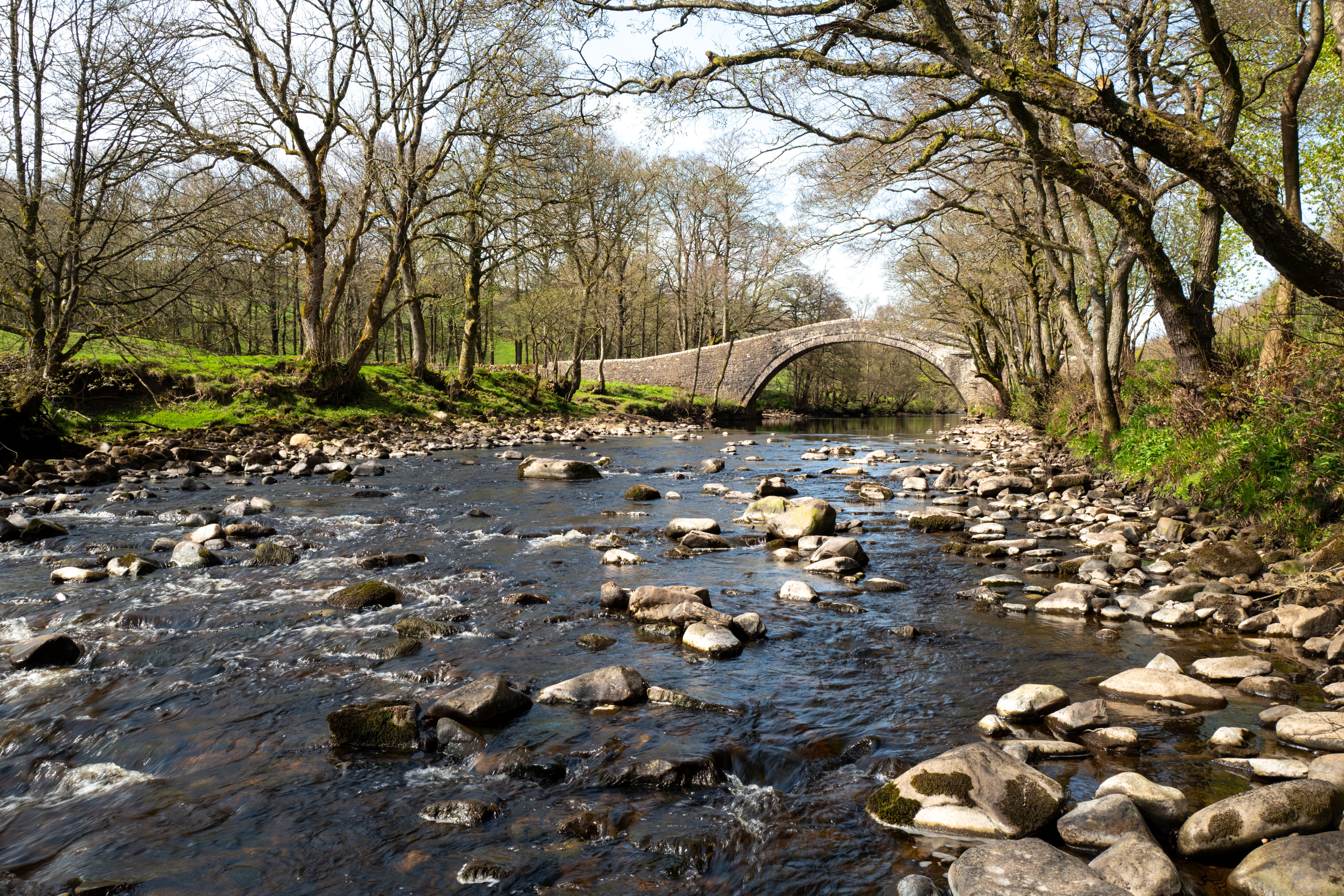 Beautiful Ivelet Bridge spanning a rocky river surrounded by trees in Yorkshire, England.