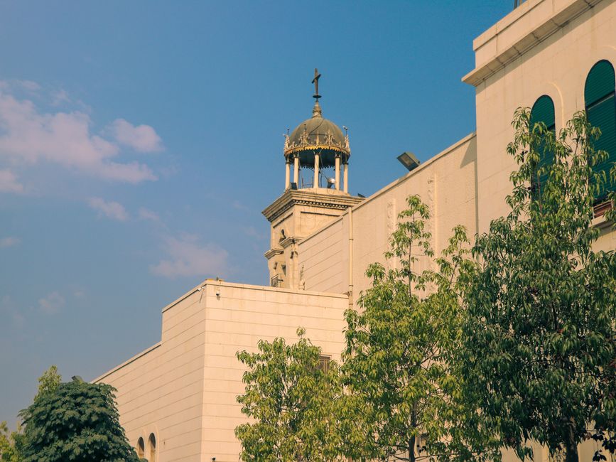 A historic church tower with a dome in Damascus, surrounded by greenery under a clear sky.