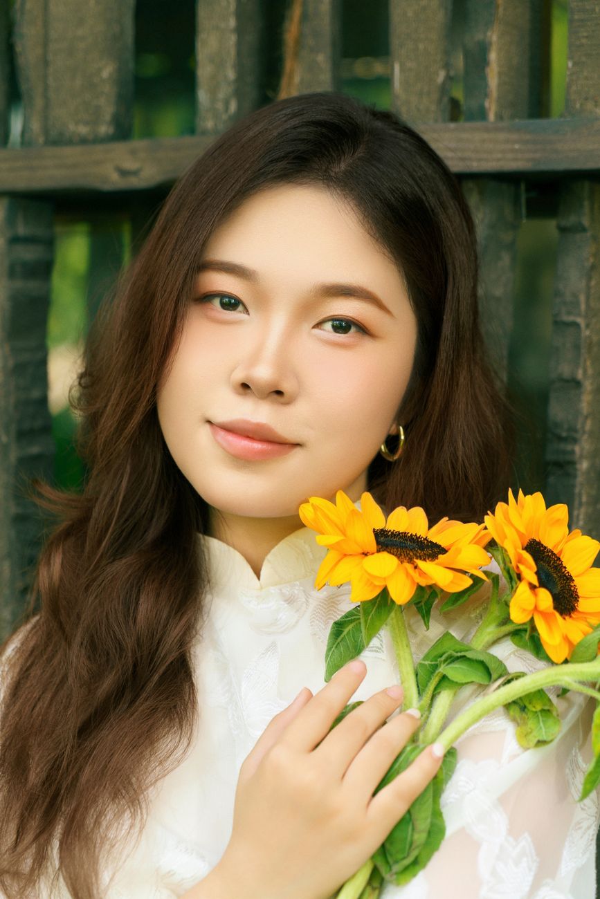 A young Vietnamese woman in traditional dress holding sunflowers in an outdoor portrait.