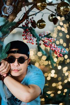 Man with sunglasses leaning on decorated tree branch, holiday theme.