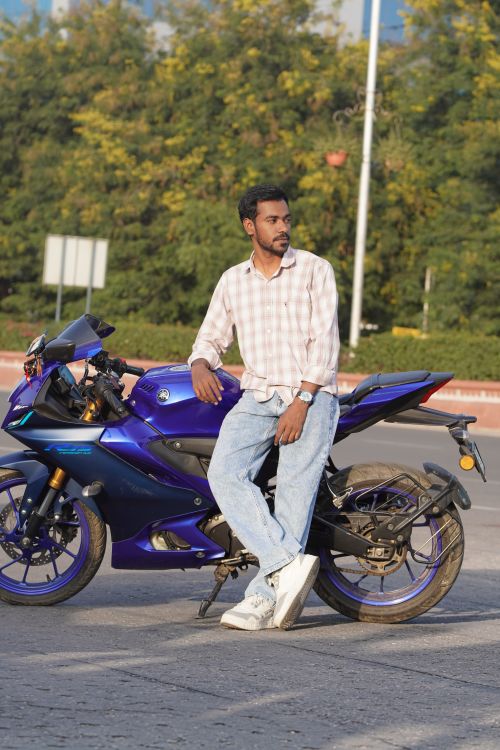 Free Young man leaning against a blue motorcycle in a sunny outdoor setting. Stock Photo