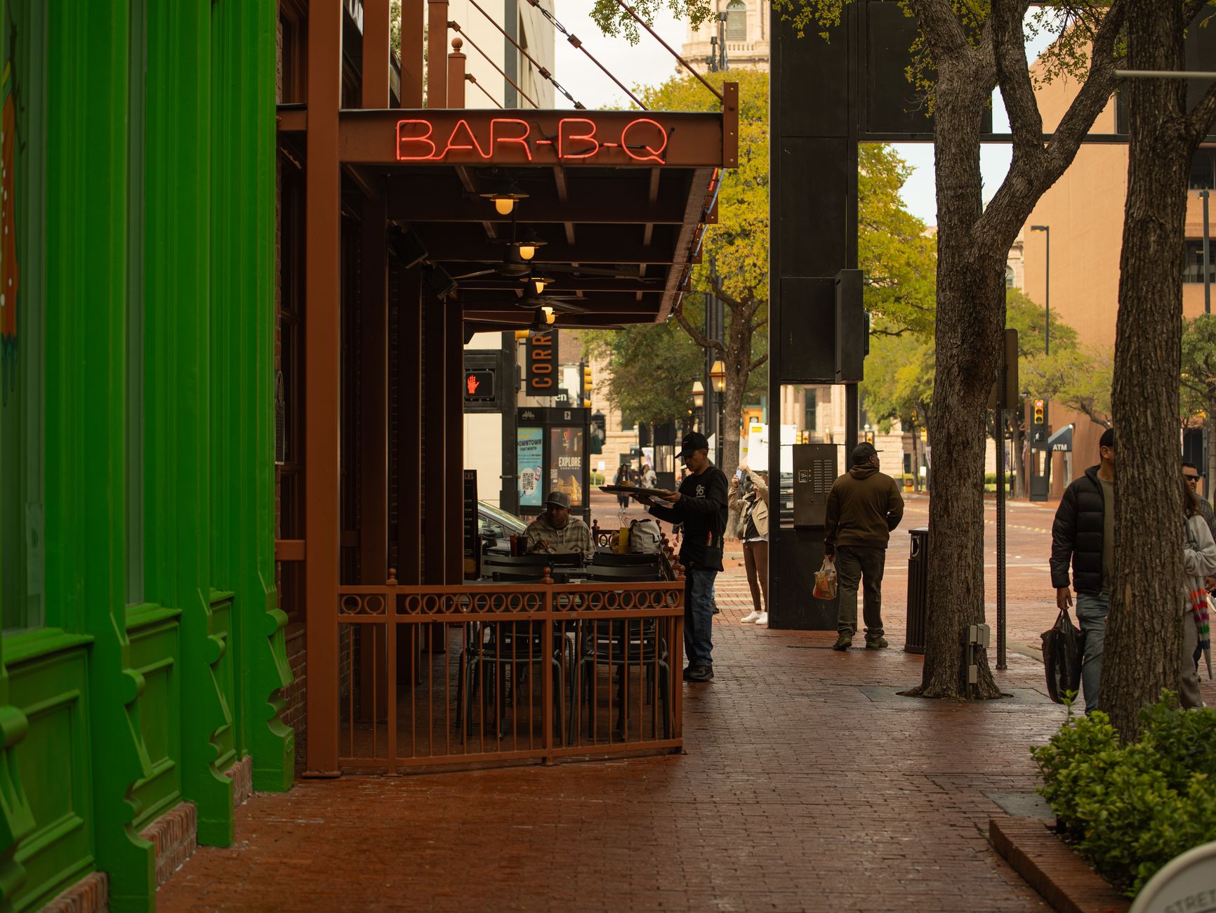 Downtown street with BAR-B-Q sign and people enjoying a city vibe.