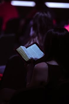 A young woman engrossed in reading a book while seated in a dimly lit room, captured in Jakarta.