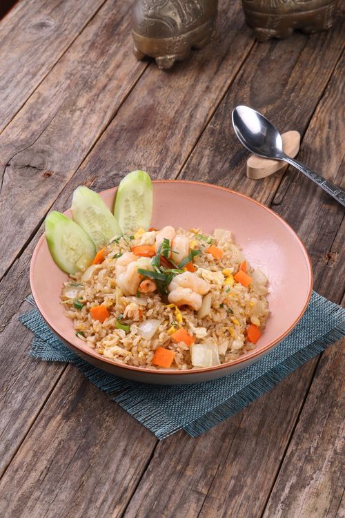 Free Mouth-watering shrimp fried rice served with fresh cucumber slices in a rustic setting. Stock Photo