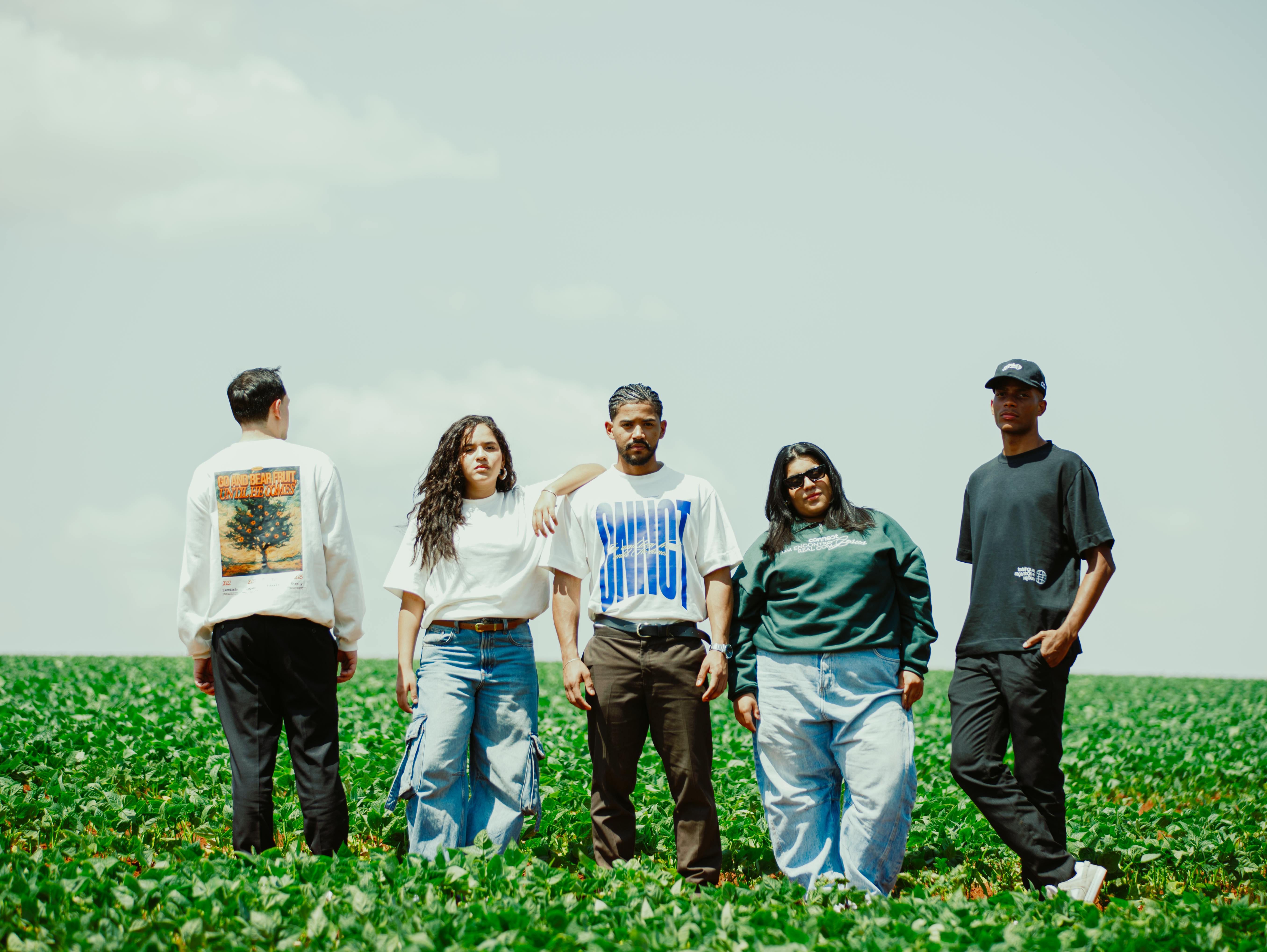 Five young adults stand confidently in a green field under a clear sky.