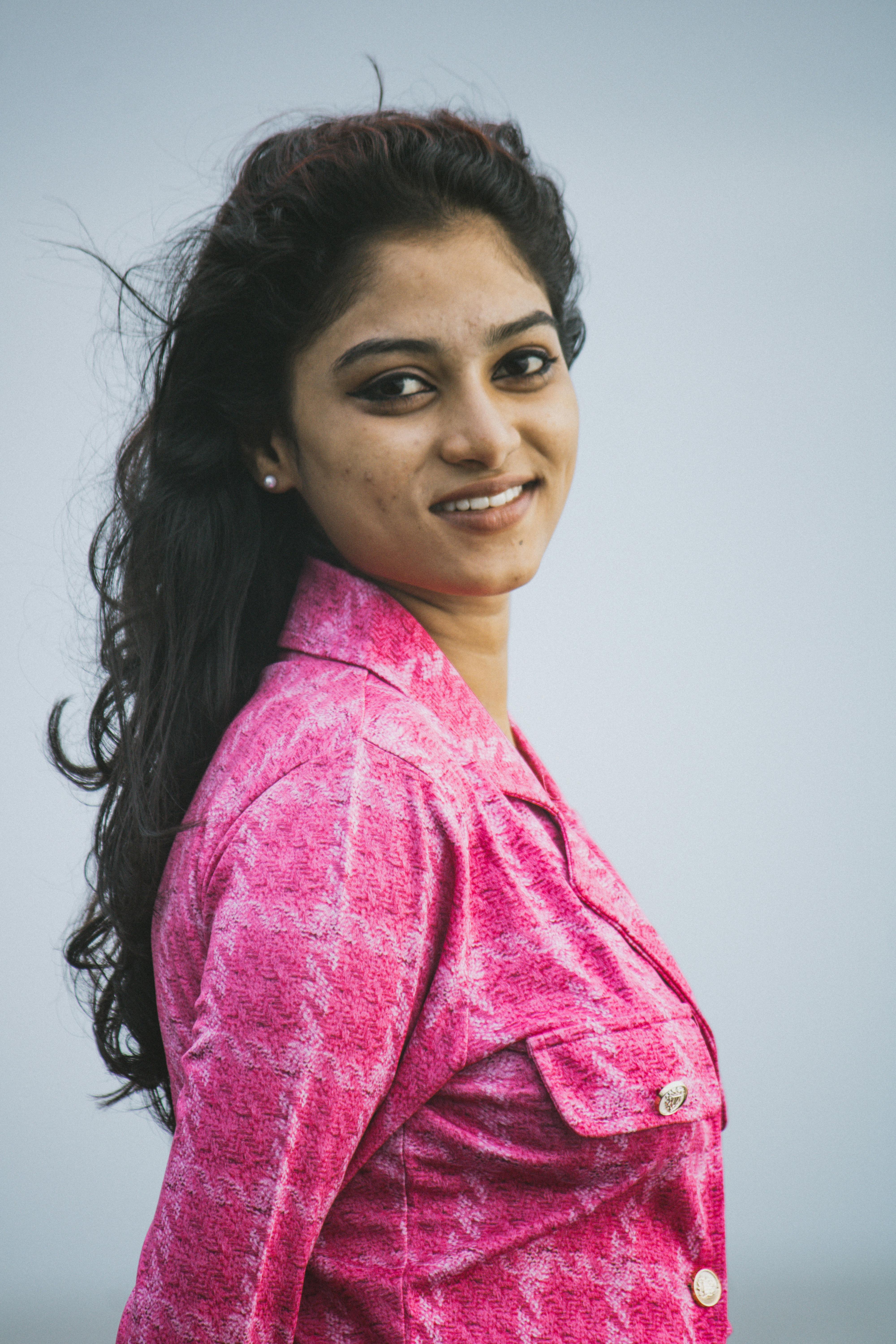 Smiling woman in a pink jacket outdoors on a breezy day, natural beauty.