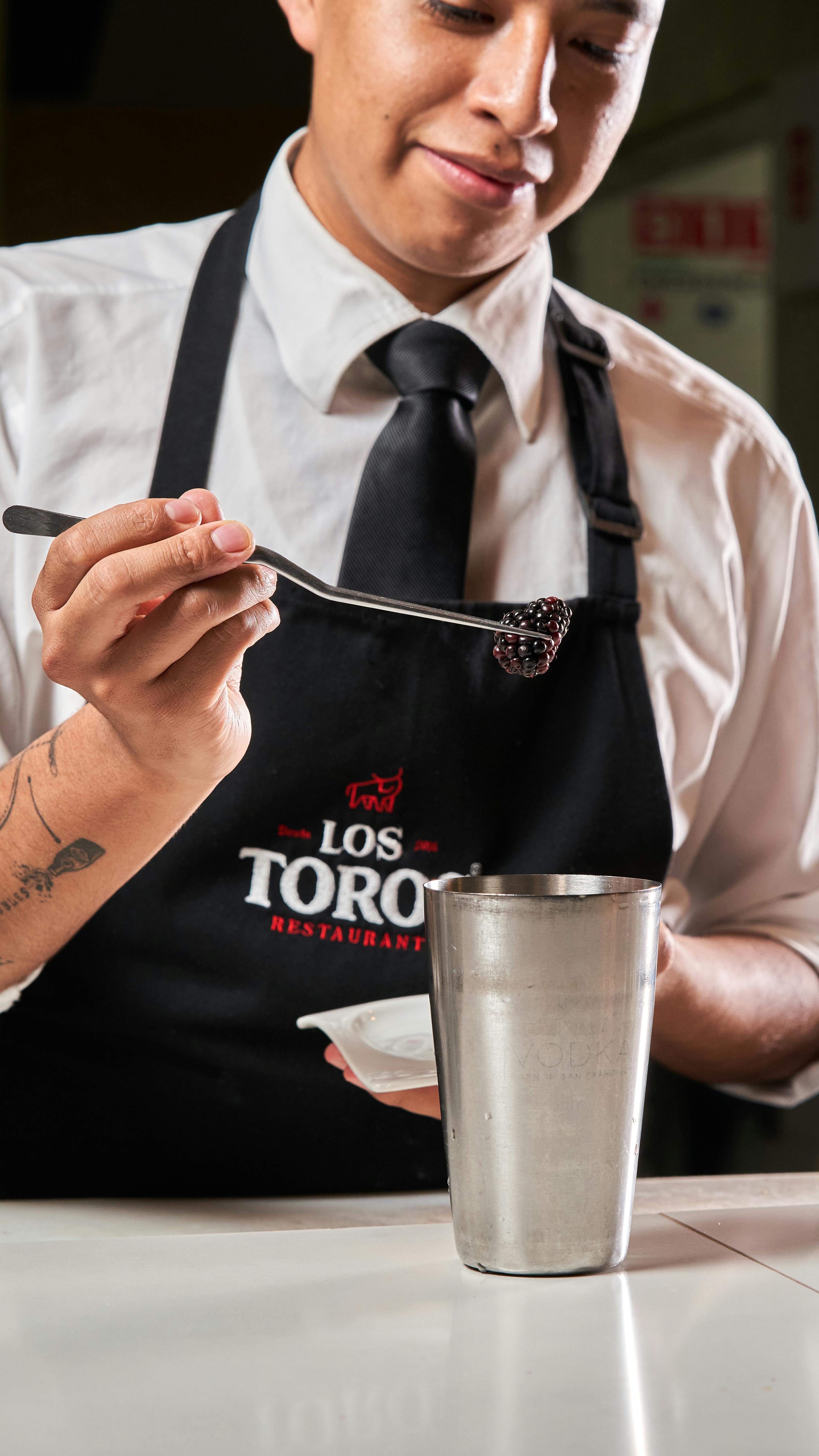 Bartender adds blackcurrants to a cocktail, showcasing skill and detail in drink preparation.