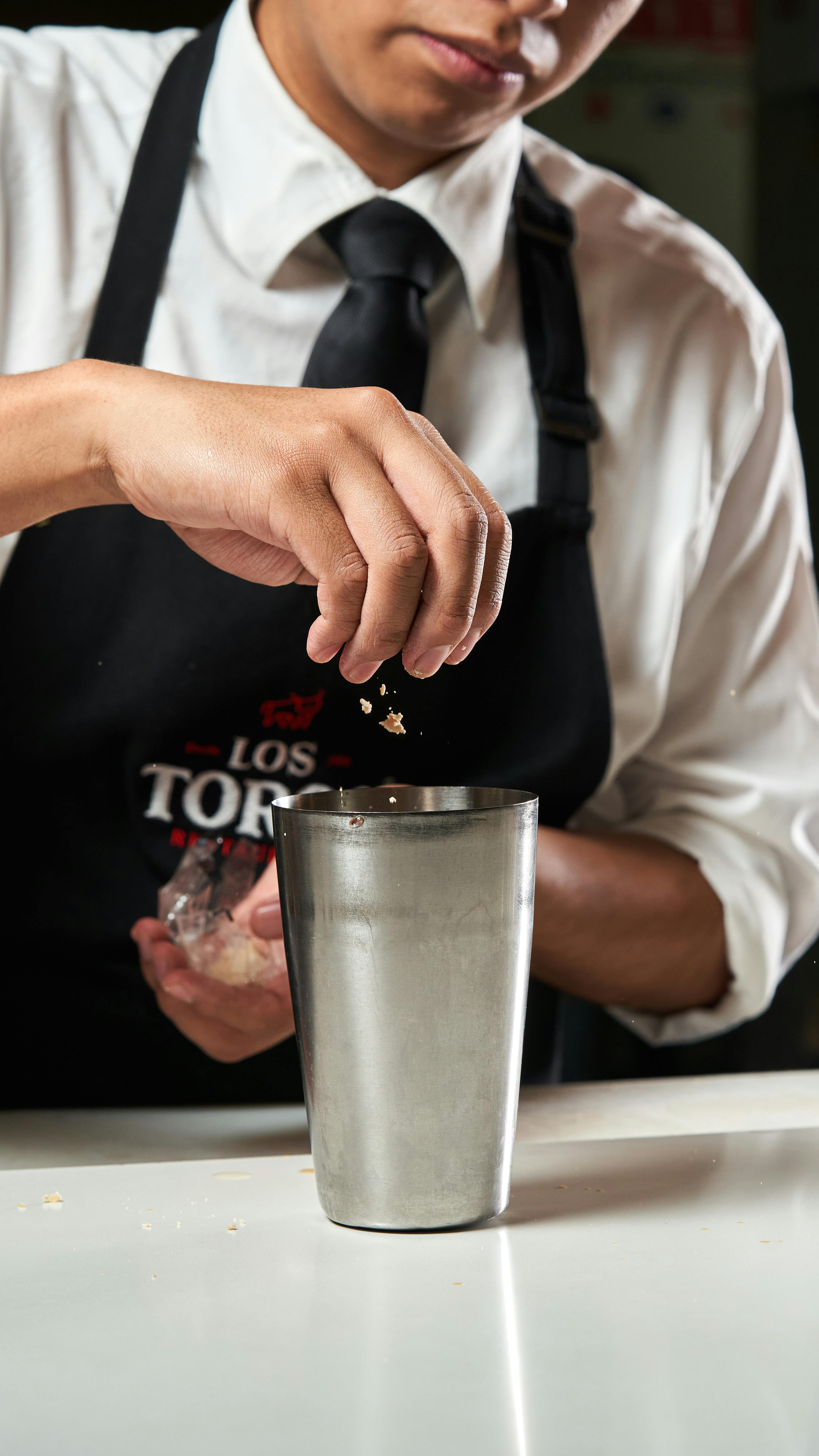 A bartender skillfully adds ingredients to a cocktail shaker, showcasing mixology expertise.