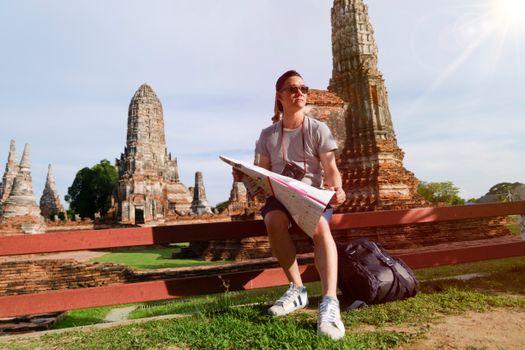 Man studying map amidst ancient temple ruins in Thailand, highlighting travel and exploration.