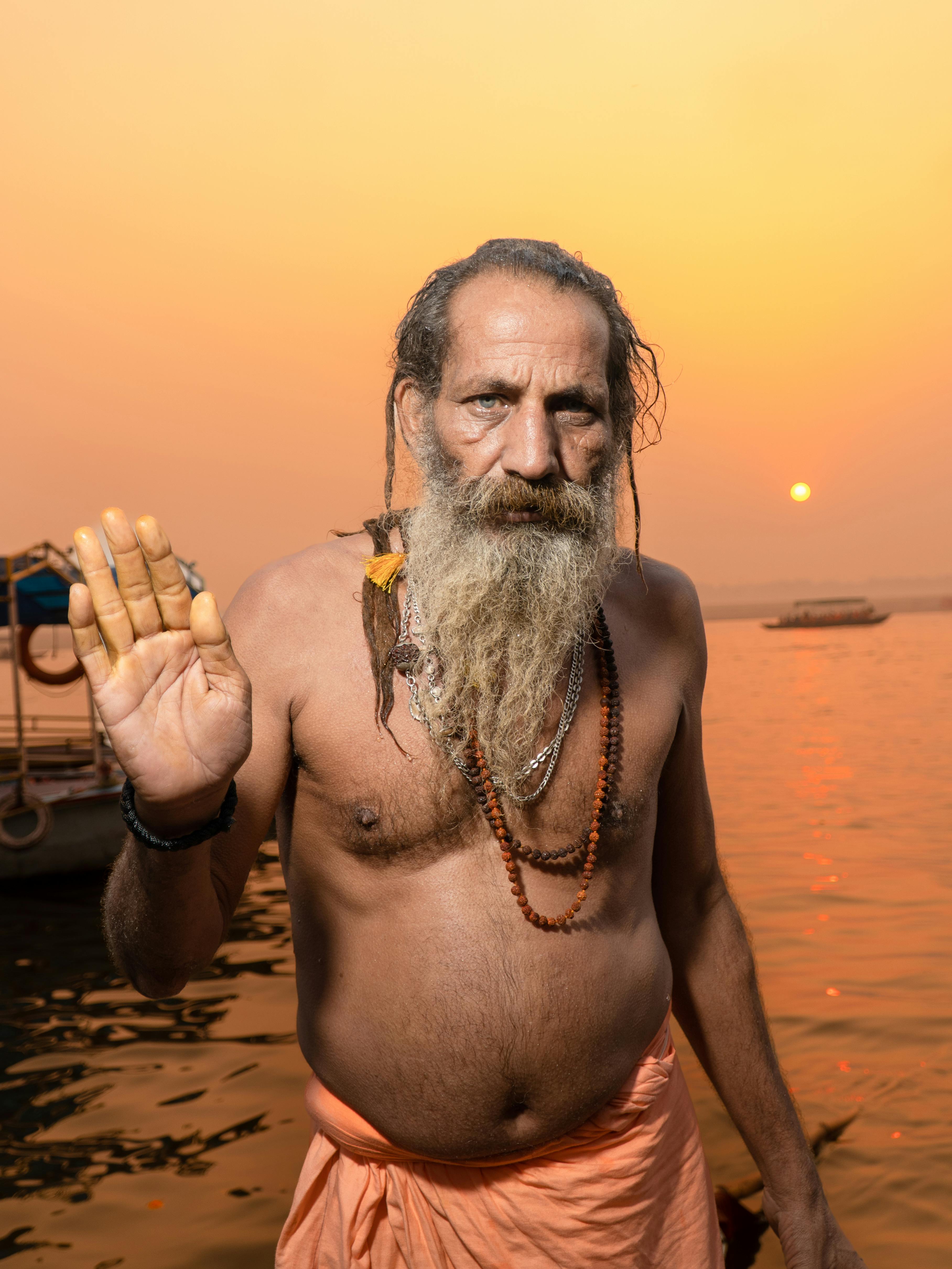 A bearded holy man offers a blessing by the Ganges River during sunset in Varanasi, India.