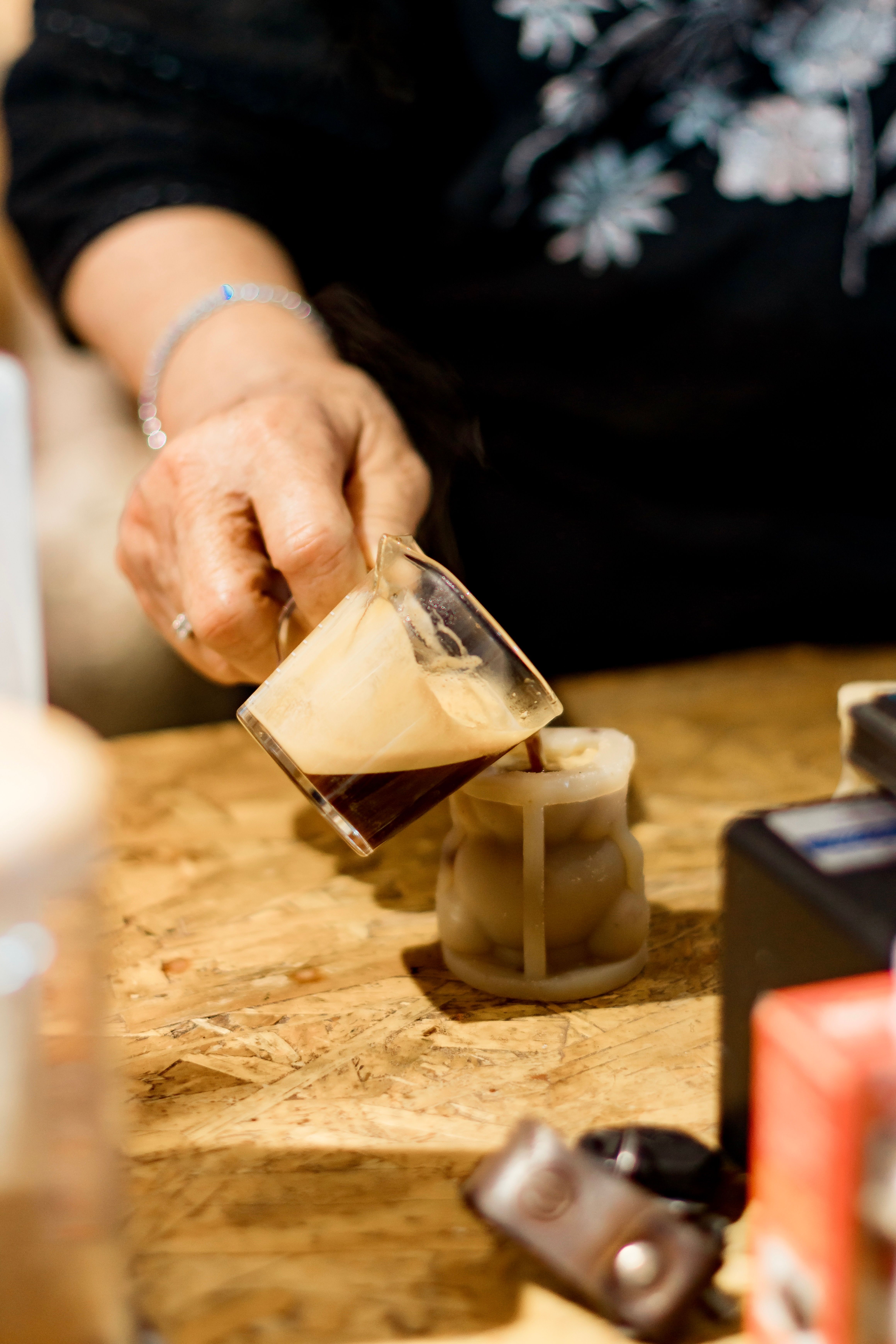 Close-up of a person pouring freshly brewed coffee into a cup on a wooden table.