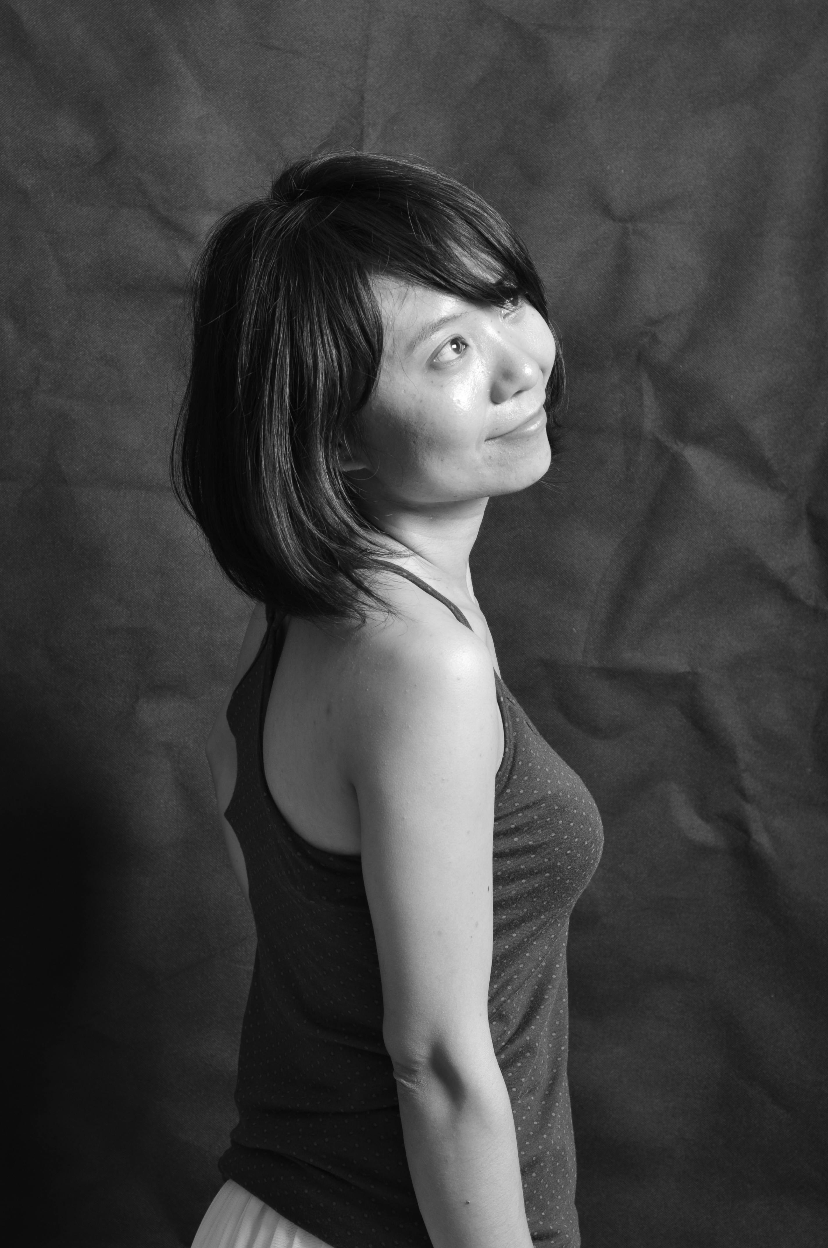 Portrait of a smiling woman in profile, standing against a textured backdrop in a studio setting.