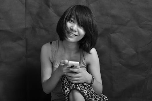 Black and white portrait of a smiling woman holding a smartphone, showcasing a casual and relaxed moment.