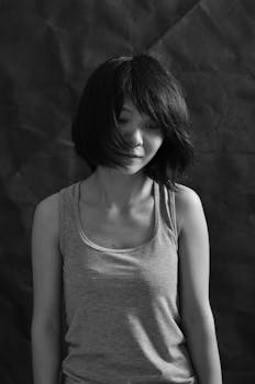 Moody black and white portrait of a young woman with short hair facing downwards, evoking introspection.