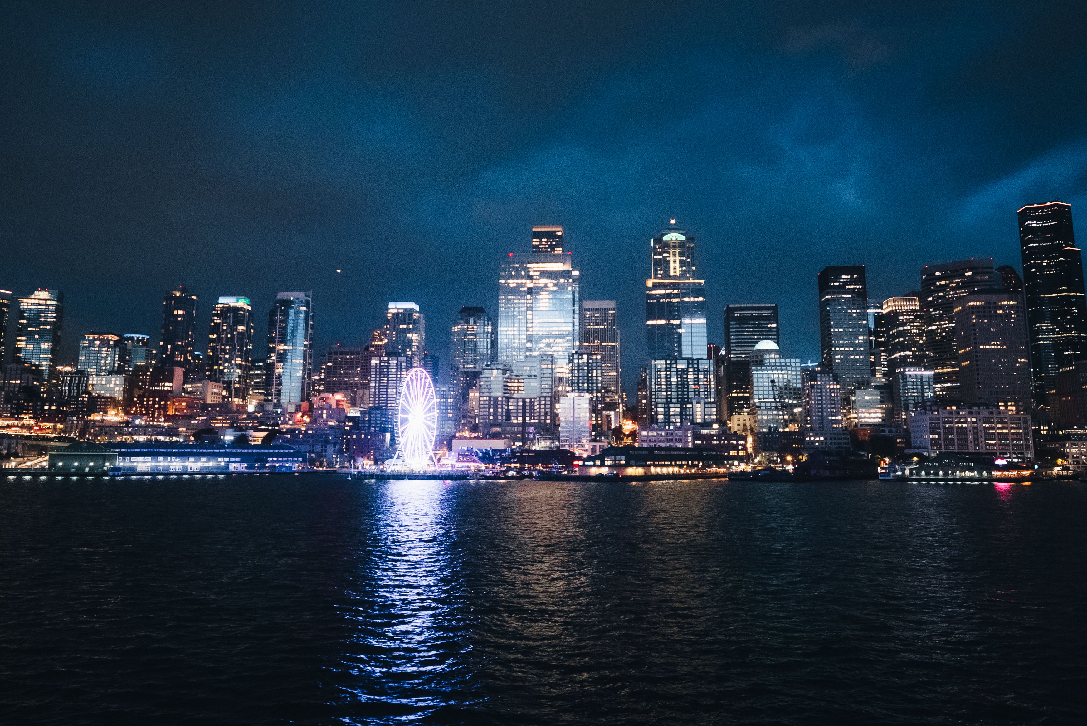 Stunning view of Seattle's illuminated skyline reflecting on the water with a Ferris wheel shining brightly at night.