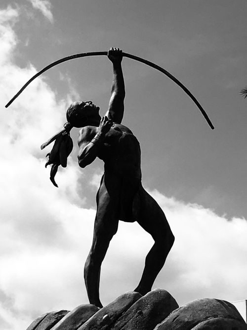 Free Black and white photo of a powerful statue of a warrior with a bow reaching towards the sky. Stock Photo