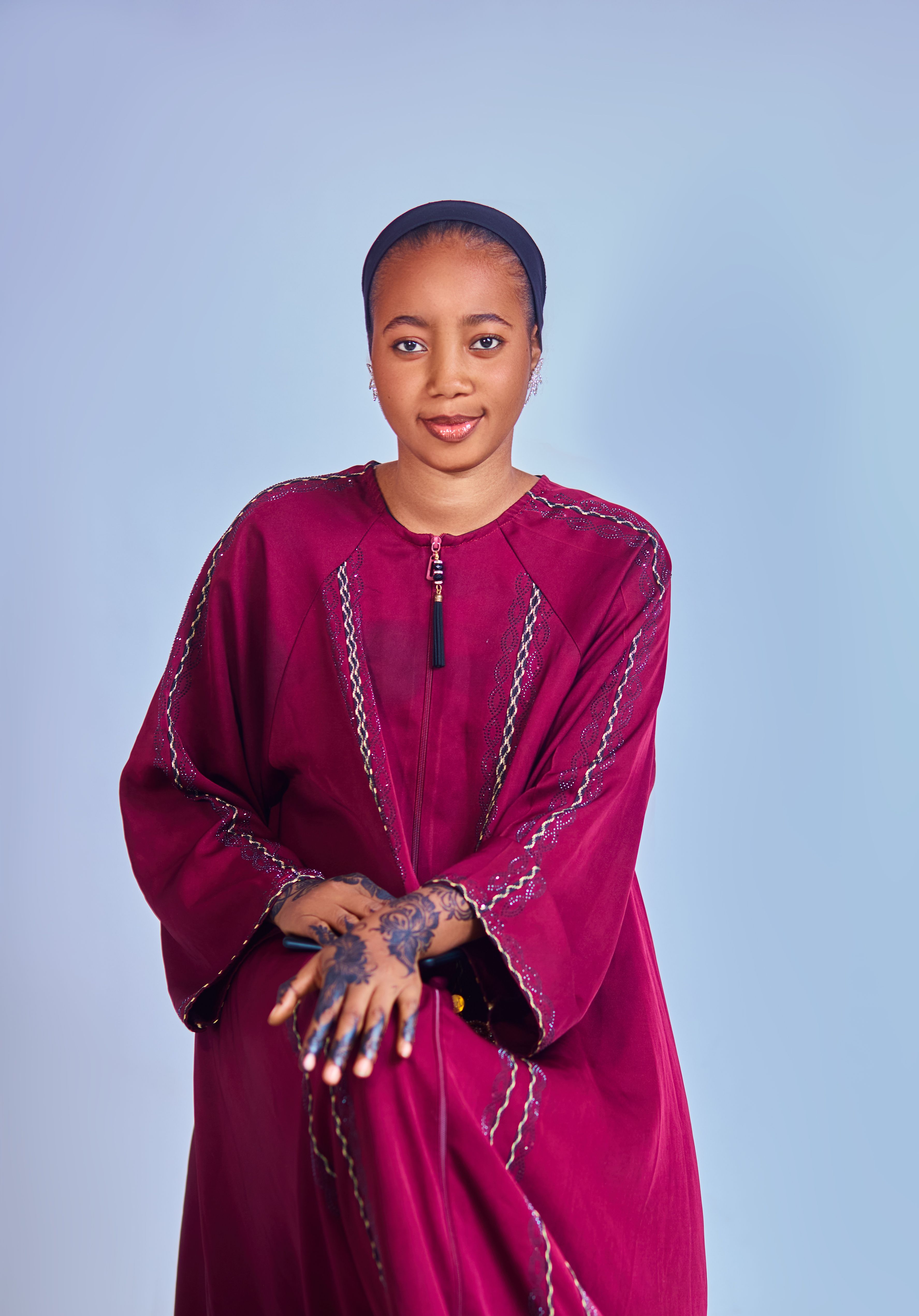 Portrait of an elegant woman wearing maroon traditional dress with intricate embroidery and henna on her hands.