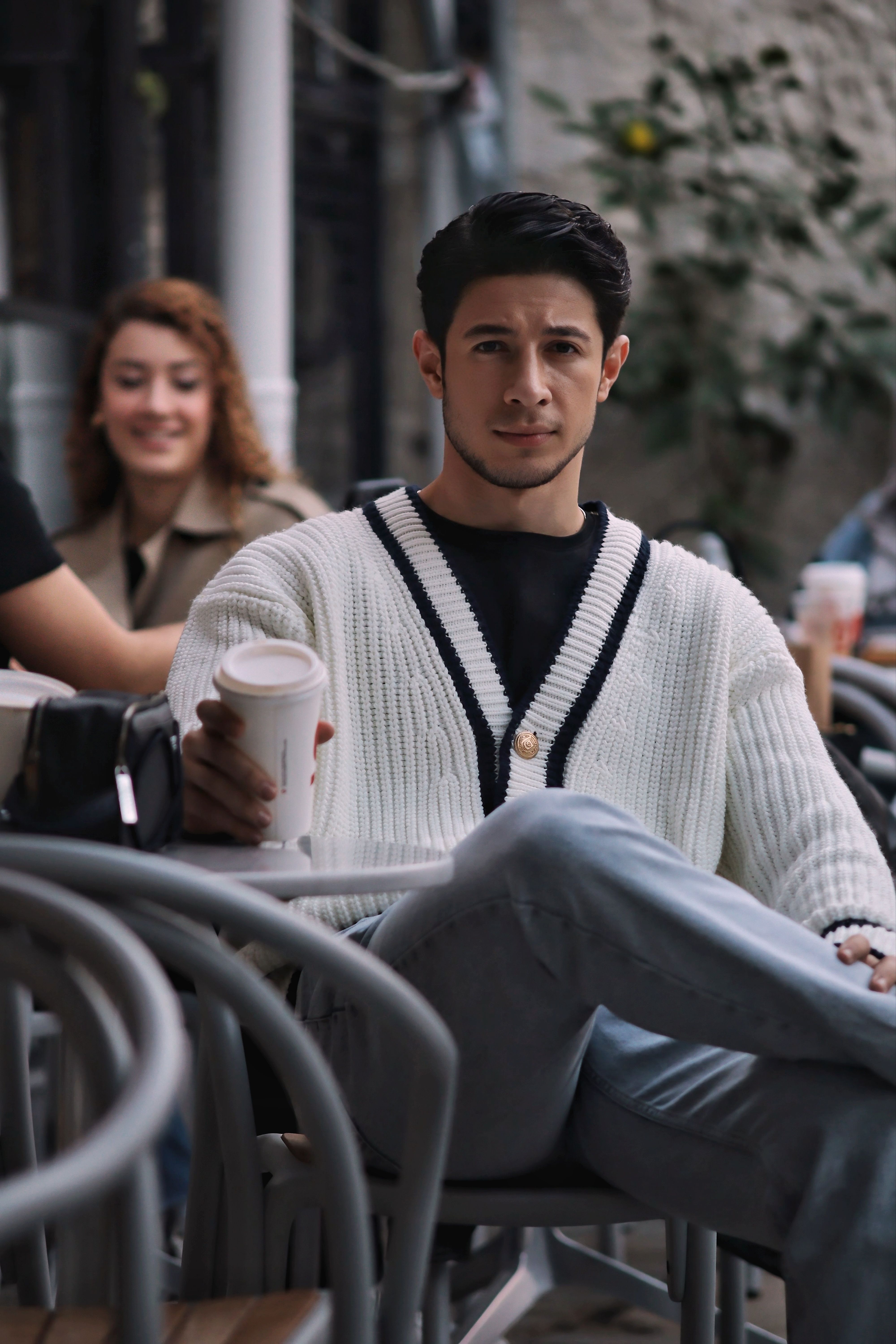 Young adults enjoying coffee at an outdoor cafe, dressed stylishly.