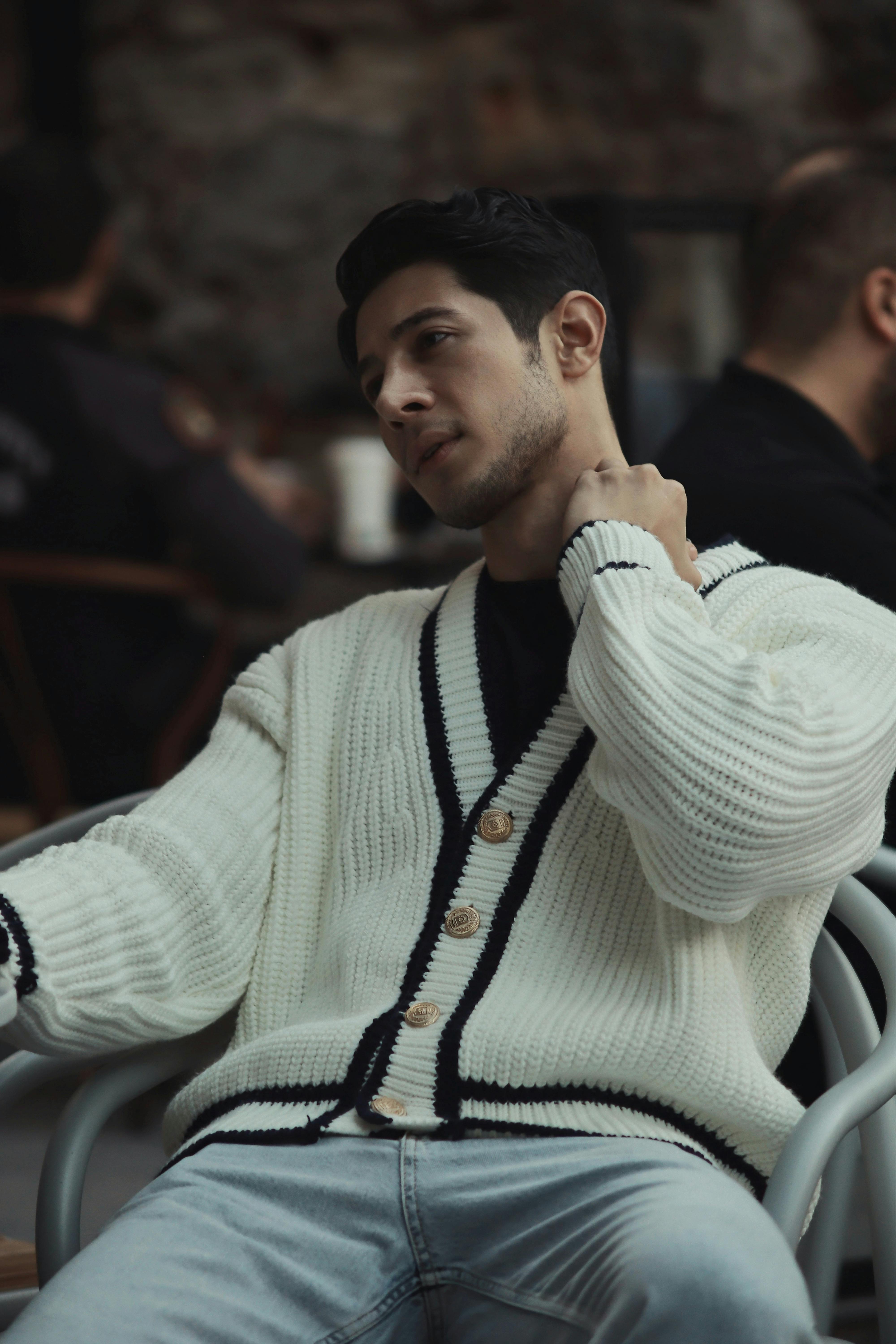 Young man in a knitted sweater relaxing in a cafe setting, embodying modern casual style.