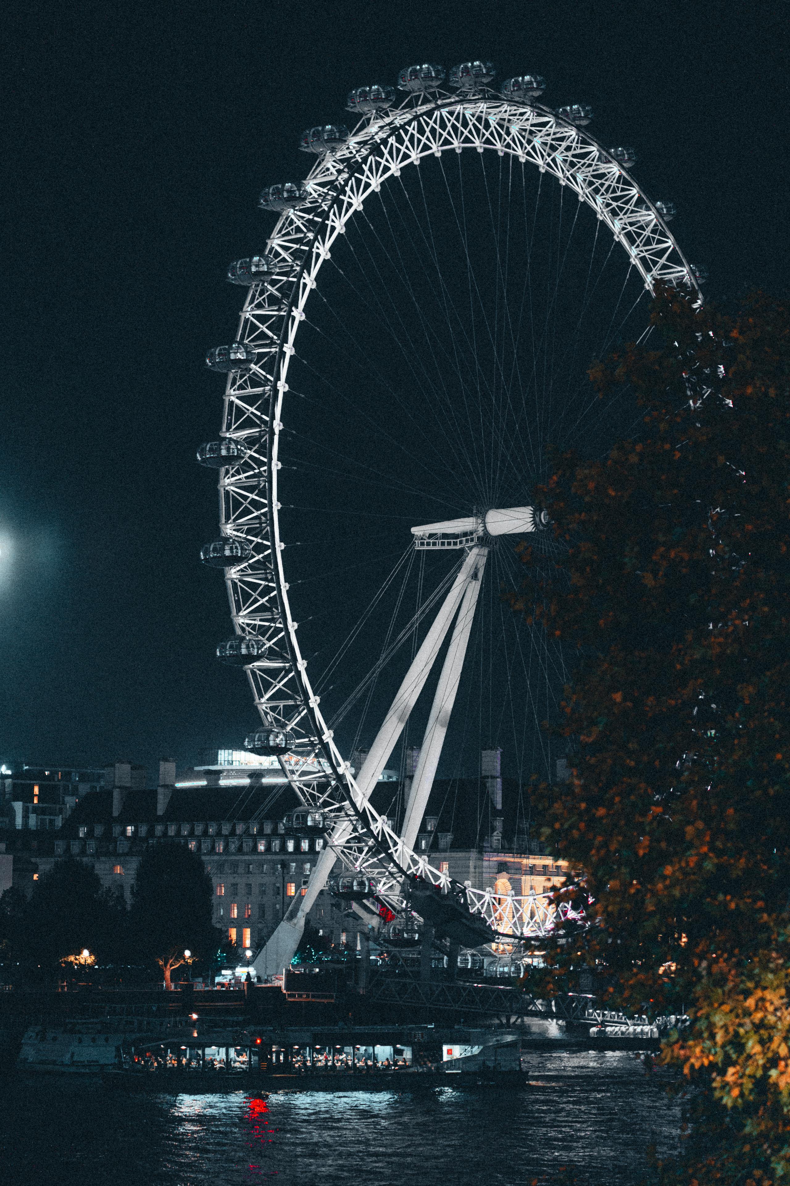 The London Eye spectacularly lit at night, overlooking Thames River with city lights.