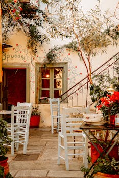A cozy Greek restaurant courtyard with white chairs and colorful flowers in Athens, Greece.