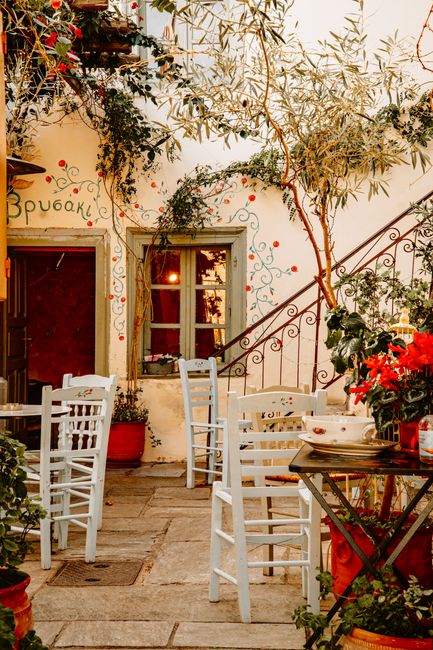 A cozy Greek restaurant courtyard with white chairs and colorful flowers in Athens, Greece.