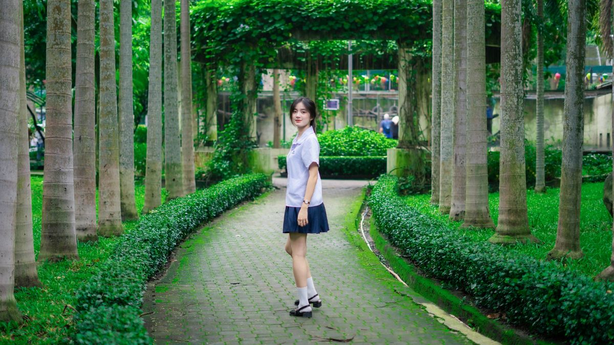 制服姿で緑の小道を歩く学生(イメージ)