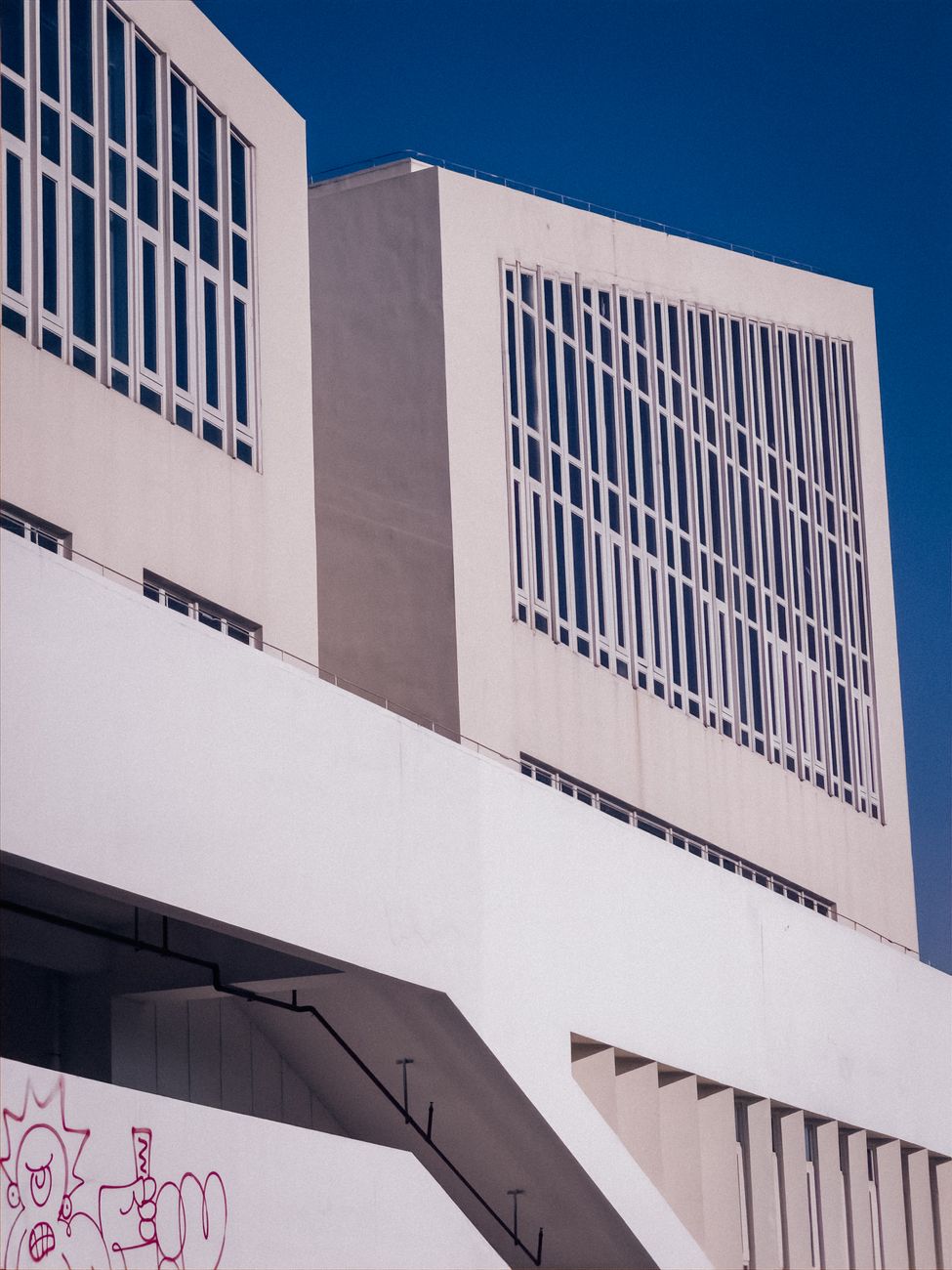 Minimalist view of a modern building facade with striking geometric lines under a clear blue sky.
