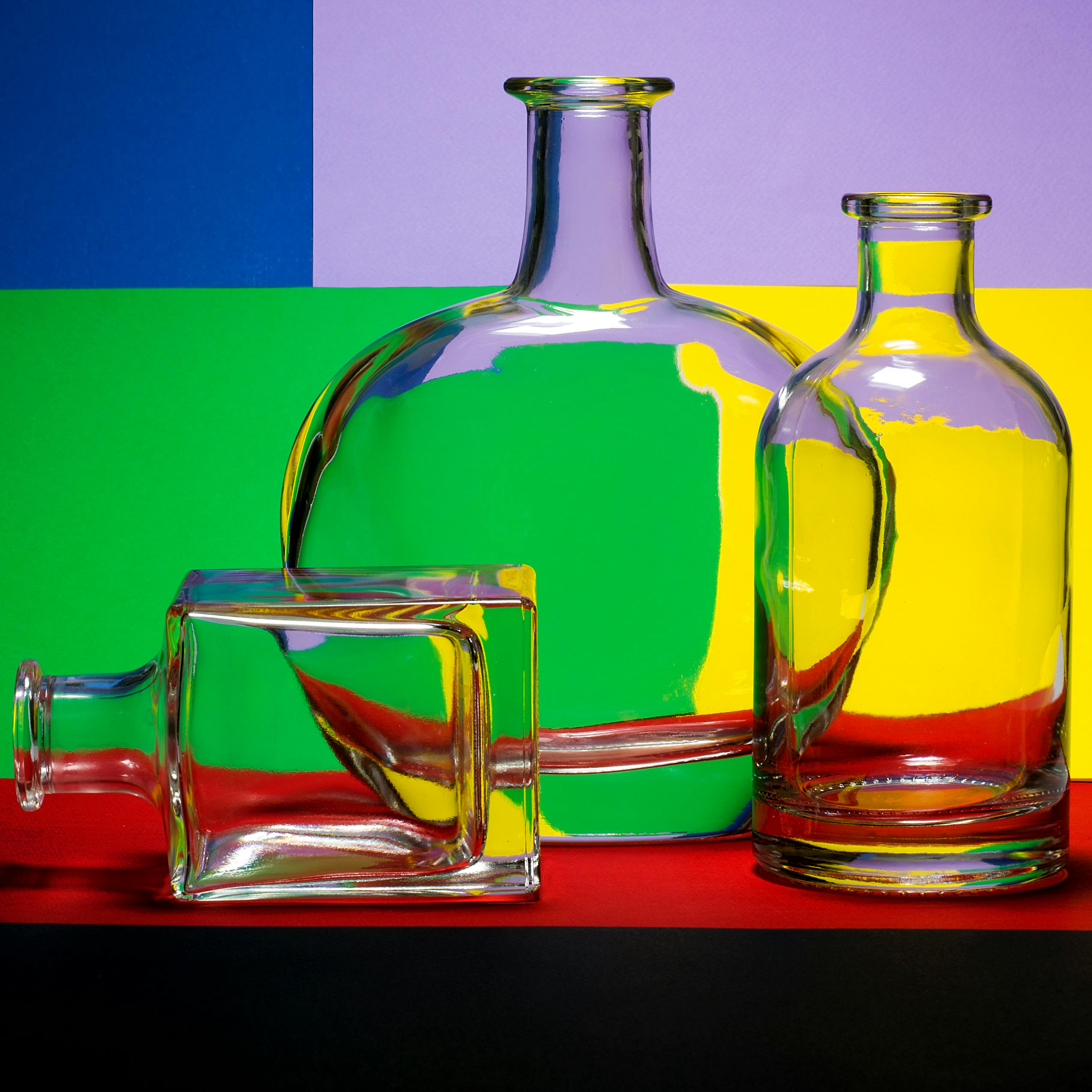 бесплатная Стеклянные бутылки с красочным геометрическим фоном создают яркую композицию натюрморта. Стоковое фото
