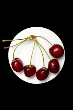 Close-up of fresh red cherries on a round plate against a black background.