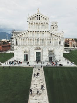 Iconic Pisa Cathedral with Leaning Tower in Italy under a cloudy sky.