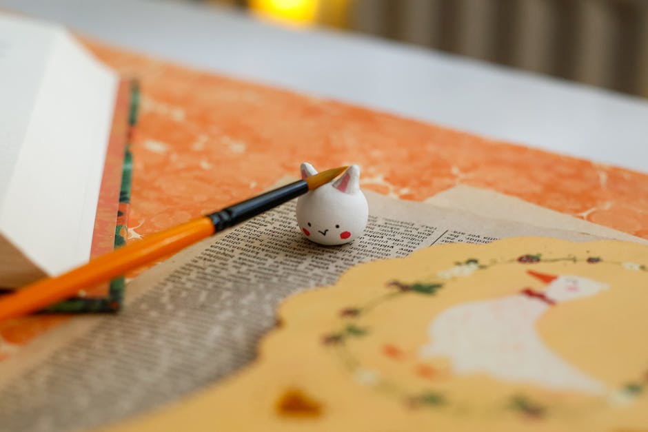 Artistic workspace with open book, paintbrush, and adorable cat figurine.