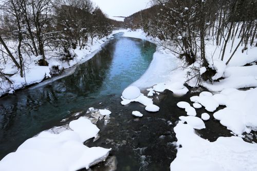 Free A tranquil winter scene showcasing a snow-covered riverbank with icy river flow. Stock Photo